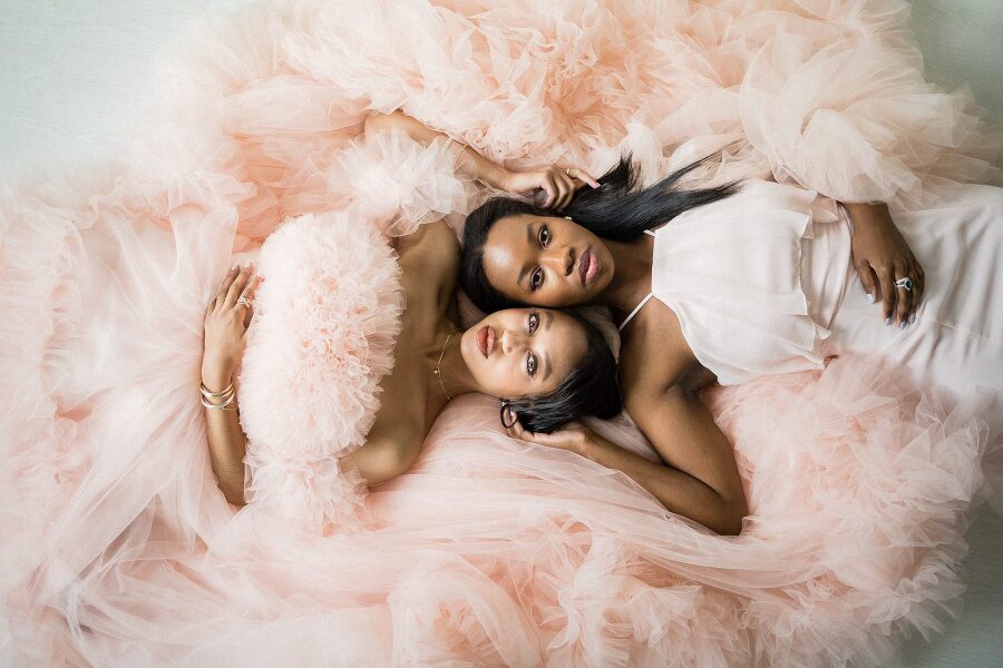 sisters lying on photo studio floor in a cloud of pink tulles with hands on each other's cheek